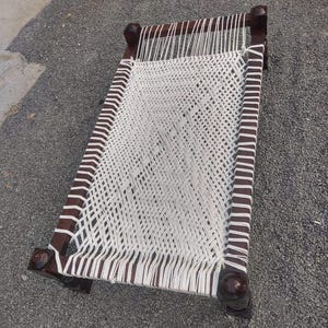 May include: A wooden frame with a white woven rope bed. The bed is made of dark wood and has a simple design.