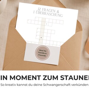 May include: A tan envelope containing a white card with a crossword puzzle and the text "12 FRAGEN & 1 &Uuml;BERRASCHUNG." A small card with the text "Ideal f&uuml;r Familie & Freunde" is also visible. The phrase "EIN MOMENT ZUM STAUNEN" is at the bottom.
