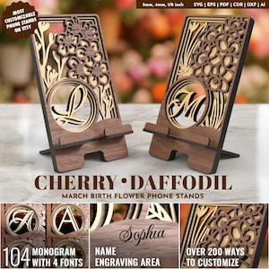 Puede incluir: Dos soportes de teléfono de madera con recortes florales e iniciales personalizadas. Los soportes son marrones con un diseño floral de madera clara. El texto en los soportes dice "Cherry Daffodil March Birth Flower Phone Stands". Personalizable.