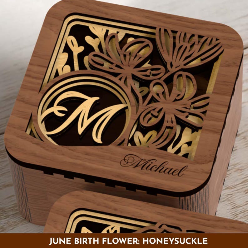 May include: Wooden box with intricate laser-cut floral design and the letter "M" in a circle. The box features the name "Michael" and the text "JUNE BIRTH FLOWER: HONEYSUCKLE". The box is made of wood with gold accents.