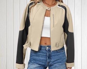 Puede incluir: Chaqueta de cuero sintético beige y negra con cuello redondo, cierre de cremallera y paneles negros en las mangas. La chaqueta tiene un corte cropped y detalles de hebilla en la cintura.