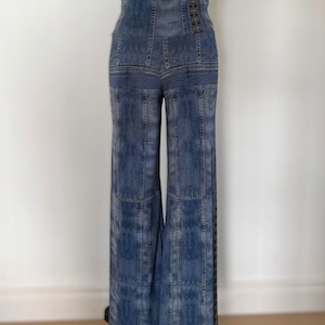 Peut inclure: Un combishort en jean présenté sur un mannequin. Il comprend un débardeur noir côtelé, un corsage en jean taille haute avec des coutures décoratives et un pantalon large. Le jean est bleu délavé avec des accents plus foncés.