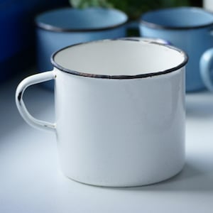 May include: White enamel mug with a black rim and a handle. The mug has a slight chip on the rim.