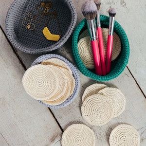 Puede incluir: Tres cuencos de crochet, uno gris, uno verde y uno gris claro, con varios artículos en su interior. El cuenco gris contiene joyas, el cuenco verde contiene pinceles de maquillaje y el cuenco gris claro contiene discos de algodón redondos de crochet.