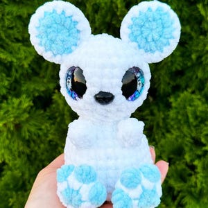 May include: A white crocheted mouse with blue ears and feet. The mouse has large, glittery eyes.