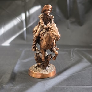 May include: A bronze-colored sculpture of a person riding a horse. The rider wears a hat and detailed clothing. The horse is rearing up, and the sculpture is mounted on a circular base. The overall theme is equestrian.