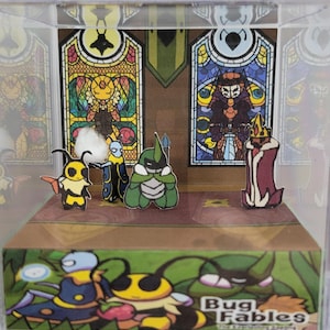 May include: A diorama featuring characters from "Bug Fables." The scene includes paper cutouts of insect-like figures on a stage with stained-glass window backdrops. The base of the display box has the game's title and illustrations of the characters.