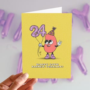 May include: A yellow birthday card with a cartoon kidney character holding two purple balloon-shaped numbers that read "24". The kidney wears a party hat and the card reads "HAPPY 24TH KIDNEY-VERSARY!"