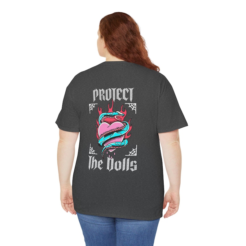 Puede incluir: Una camiseta gris oscuro jaspeada con un estampado gr&aacute;fico de un coraz&oacute;n con una serpiente enroscada a su alrededor. El coraz&oacute;n est&aacute; en llamas y el texto "Protect the Dolls" est&aacute; impreso debajo del coraz&oacute;n.