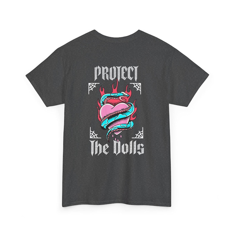 Puede incluir: Una camiseta gris oscuro con un estampado gr&aacute;fico de un coraz&oacute;n con una serpiente enroscada a su alrededor, llamas detr&aacute;s del coraz&oacute;n y el texto "PROTECT THE DOLLS" en blanco.
