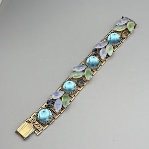 May include: A vintage gold-tone bracelet featuring large, round, light blue cabochon stones interspersed with smaller, oval and marquise-shaped stones in shades of blue and green. The bracelet has a rectangular link design and a fold-over clasp.