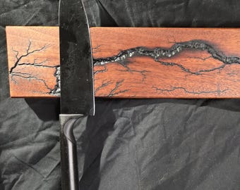 May include: A wooden magnetic knife holder with a black, lightning-shaped design. A black kitchen knife is attached to the holder.