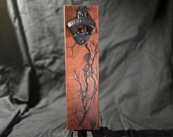 May include: A wooden bottle opener with a black metal opener attached. The wood has a dark brown color with black lightning-like patterns.