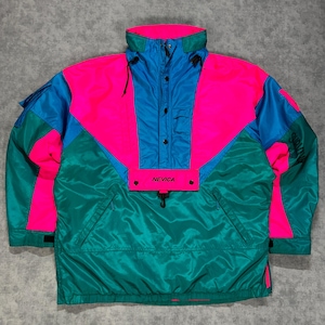 May include: A color-blocked pullover jacket featuring vibrant panels of hot pink, bright blue, and teal green. The jacket has a high collar, a central placket with snap buttons, and a front flap pocket with the black text NEVICA printed on it.