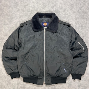 May include: A black bomber jacket featuring a dark faux fur collar, a full-length silver metal front zip, and ribbed cuffs and hem. The jacket includes shoulder epaulets, two front snap-button pockets, and a zipped utility pocket on the sleeve.