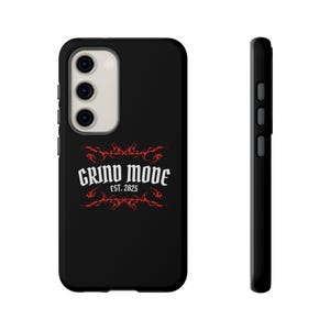 May include: Black phone case with a red tribal design and the words "GRIND MODE EST. 2025" in white. The case has a camera cutout and side buttons. The phone case is shown from the front and side.