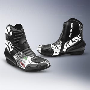 Puede incluir: Par de botas de moto en blanco y negro con un diseño del Joker. Las botas son de caña alta con cierre de hebilla y la palabra "RIVALION" impresa en el lateral. Las botas tienen suela negra.