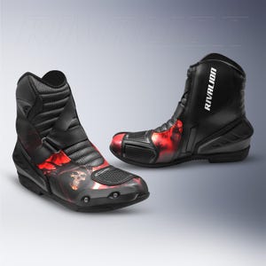 Puede incluir: Botas de moto negras con gráficos de llamas rojas y calaveras. Las botas tienen una cremallera lateral y hebilla. El nombre de la marca "RIVALION" está impreso en el lateral.