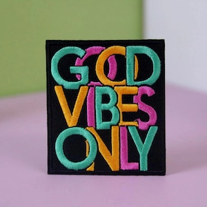 Puede incluir: Un parche bordado negro con el texto "GOOD VIBES ONLY" en letras de colores. Las letras están en un estilo superpuesto y superpuesto. Los colores son rosa, amarillo y turquesa.