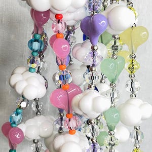 May include: A colorful beaded necklace with white cloud and heart charms. The necklace features a variety of beads in shades of pink, purple, green, yellow, and blue.