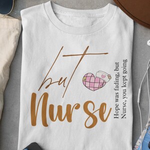 May include: White t-shirt with brown text that reads "but nurse" and a pink heart with a nurse's cap on it. The text on the right side of the shirt reads "Hope was fading, but Nurse, you kept going."