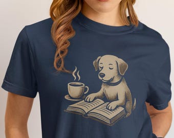 Può includere: T-shirt blu navy con un cane dei cartoni animati che legge un libro e una tazza di caffè. Il cane è marrone chiaro con un collare nero. Il libro e la tazza di caffè sono marrone chiaro. La maglietta è di colore blu navy.