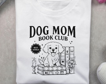 May include: White t-shirt with a black graphic that reads "DOG MOM BOOK CLUB." The design features a cartoon dog sitting on books, with a candle, flowers, and the words "BEST WORLD" and "LOVE PAWS."