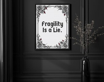 May include: A framed print displaying the phrase "Fragility Is a Lie." The design includes a white background, a black border, and illustrations of grey roses with red accents and thorny vines.