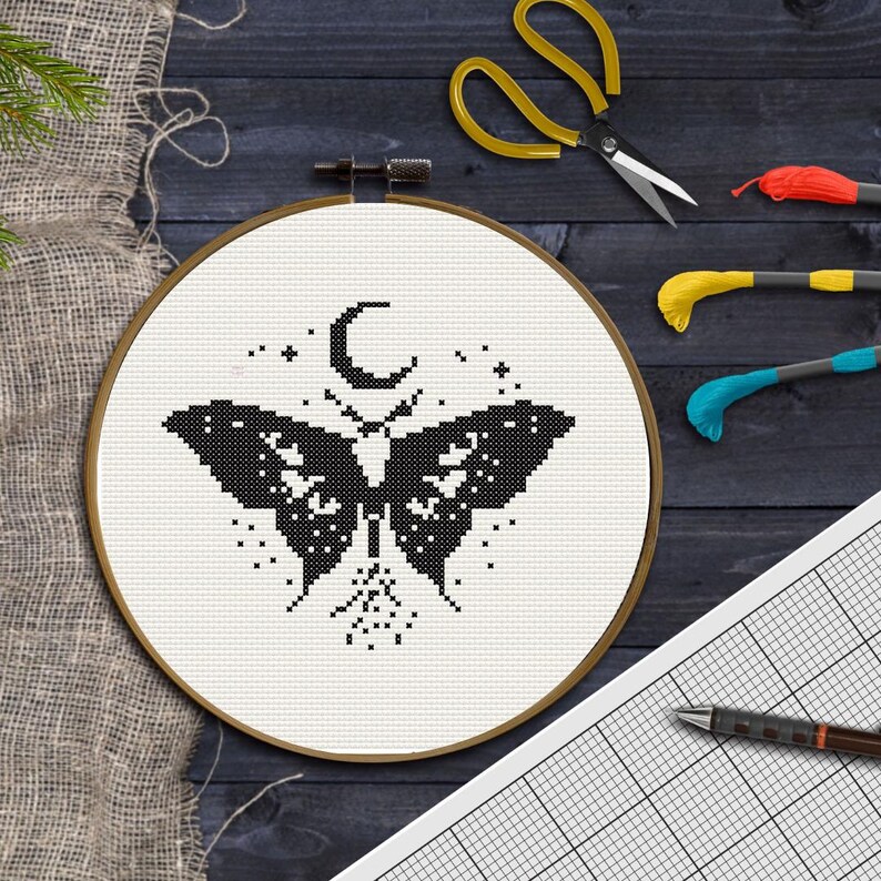 Pu&ograve; includere: Telaio da ricamo a punto croce con un disegno di farfalla in bianco e nero, una luna crescente e stelle. Include filo da ricamo, forbici e carta quadrettata con una penna. Il telaio ha un diametro di circa 20 cm.