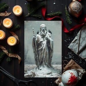 May include: A winter-themed still life featuring a print of a snow-covered statue with a staff and two ravens. The scene includes lit candles, a gold ornament, red ribbon, and a decorative paper with a spoon, all arranged on a dark wooden surface.