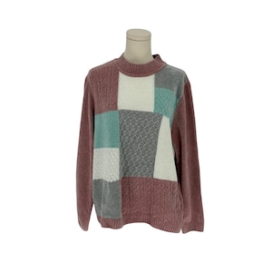 Puede incluir: Un suéter patchwork en tonos malva, gris, verde azulado y blanco. El suéter tiene cuello redondo y mangas largas. El panel frontal presenta un diseño geométrico con varios cuadrados texturizados.