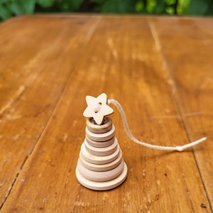 May include: A wooden toy stacking tower with a star-shaped top and a string attached. The tower is made of six round wooden pieces that stack on top of each other.
