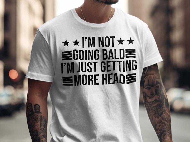 May include: White t-shirt with black text that reads "I'm not going bald I'm just getting more head" with three stars and three stripes on each side of the text.