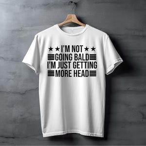 May include: White t-shirt with black text that reads "I'm not going bald I'm just getting more head" with three stars on each side of the text.