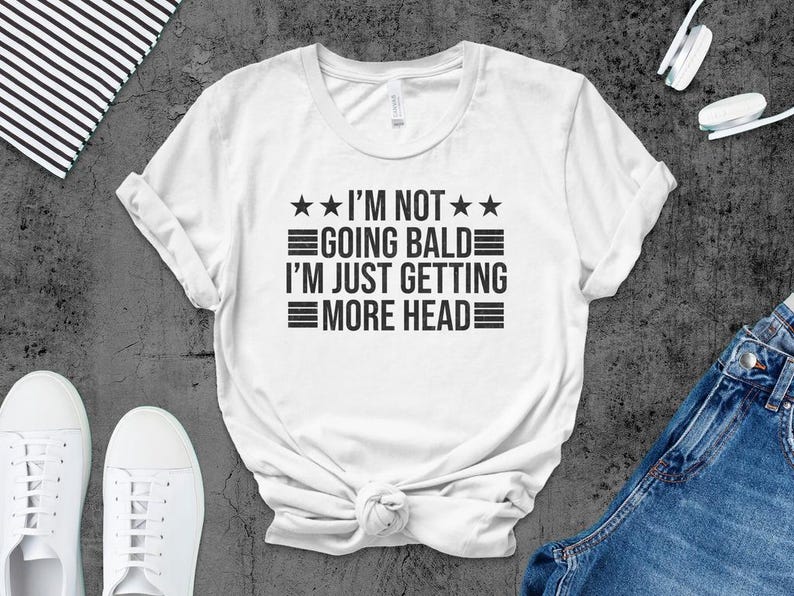 May include: White t-shirt with black text that reads "I'm not going bald I'm just getting more head" with three stars above and below the text.
