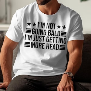 May include: White t-shirt with black text that reads "I'm not going bald I'm just getting more head" with three stars on each side of the text.
