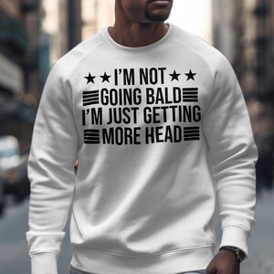 May include: White sweatshirt with black text that reads "I'm not going bald I'm just getting more head" with three stars on each side of the text.