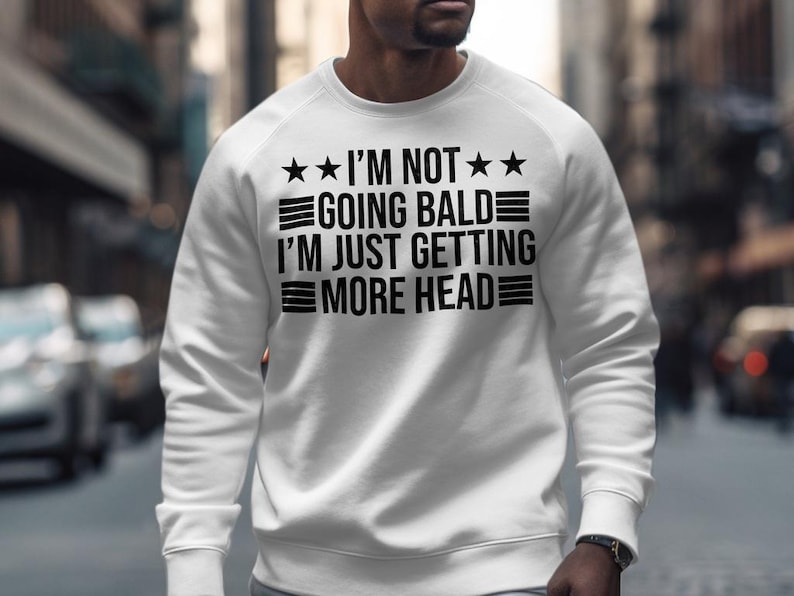 May include: White sweatshirt with black text that reads "I'm not going bald I'm just getting more head" with three stars on each side of the text.