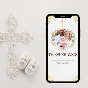 May include: A white lace cross, baby shoes, and a smartphone displaying a baptism invitation. The invitation features a family photo, gold accents, and the text "TE ESPERAMOS". The shoes have gold crosses.