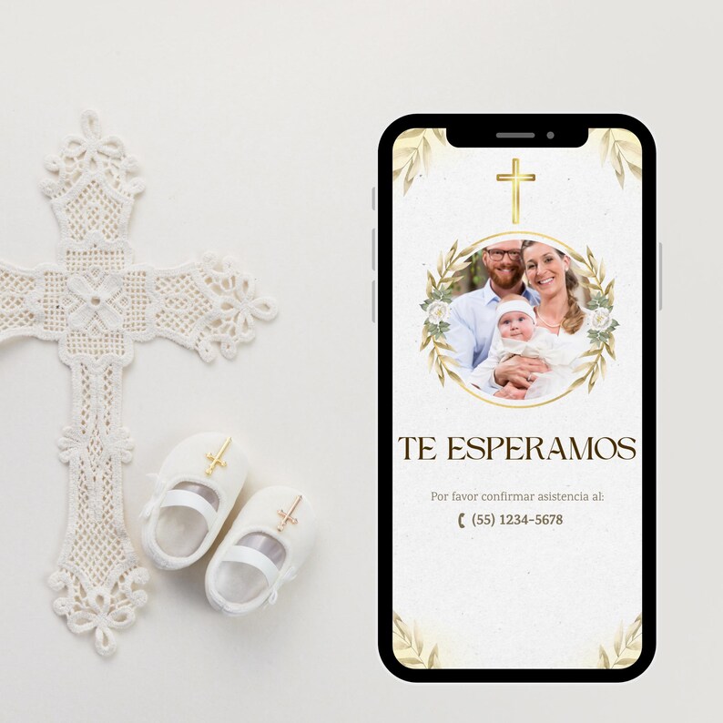 May include: A white lace cross, baby shoes, and a smartphone displaying a baptism invitation. The invitation features a family photo, gold accents, and the text "TE ESPERAMOS". The shoes have gold crosses.