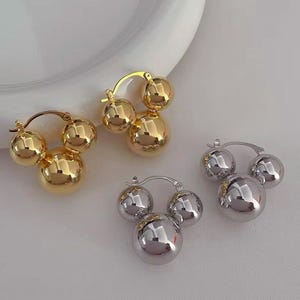 May include: Two pairs of hoop earrings with three round balls hanging from each hoop. One pair is gold and the other is silver.