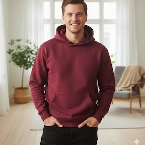 Peut inclure: Un sweat à capuche bordeaux uni avec une poche kangourou. Le sweat-shirt à capuche est de couleur unie et possède un cordon de serrage. La personne porte un jean noir et a les mains dans les poches.