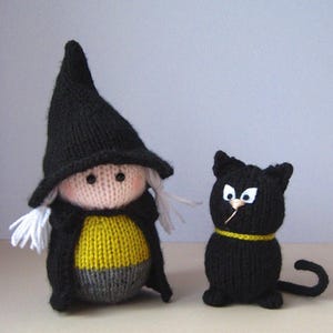May include: A knitted doll dressed as a witch in a black pointed hat, black cape, yellow shirt, and gray skirt, accompanied by a small black knitted cat with white felt eyes, a gold collar, and a long tail, both crafted from soft yarn.