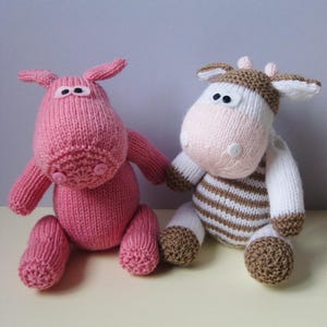 Könnte beinhalten: Zwei handgestrickte Stofftiere. Eines ist ein einfarbig rosa Wesen mit Knopfaugen und einer Knopfnase. Das andere ist ein weiß-braun gestreiftes Wesen mit einer hellrosa Schnauze, kleinen Hörnern und schwarzen Knopfaugen. Beide haben weiche Texturen.