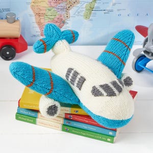 May include: A knitted toy airplane featuring a cream-colored body with bright blue wings and tail sections. The wings are accented with thin orange stripes, while the cockpit windows are represented by grey knitted patches on the front fuselage.