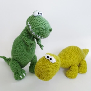 May include: Two knitted dinosaur toys. One is a standing green dinosaur with white stitched teeth and white eyes. The other is a crouching yellow-green dinosaur with white eyes. Both are made of yarn with visible knit stitches and textures.