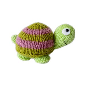 May include: A knitted turtle toy featuring a rounded shell with alternating horizontal stripes of olive green and dusty pink yarn. The head, legs, and tail are a solid light lime green. The turtle has a white felt eye patch with a black bead pupil.
