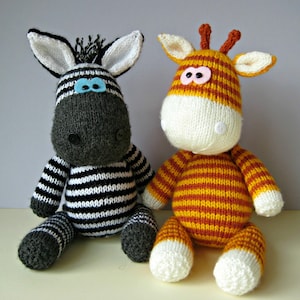 May include: Two handmade knitted stuffed animals, a zebra and a giraffe. The zebra has black and white stripes, a dark grey face, and light blue felt eyes. The giraffe has orange and yellow stripes, a white face, and small brown horns.