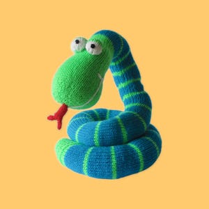 Op de afbeelding: Een gebreid slangen speelgoed in groen en blauw. De slang heeft een groene kop met grote witte ogen en een rode tong. Het lichaam is blauw met groene strepen, opgerold in een speelse pose.