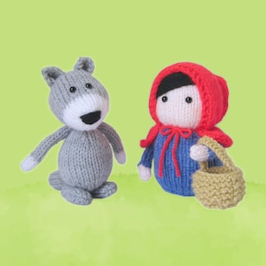 Könnte beinhalten: Zwei gestrickte Puppen, eine als grauer Wolf mit weißer Schnauze und schwarzer Nase, die andere trägt einen roten Kapuzenumhang über einem blauen Kleid und hält einen kleinen beigen Korb. Beide Puppen haben schwarze Perlenaugen.